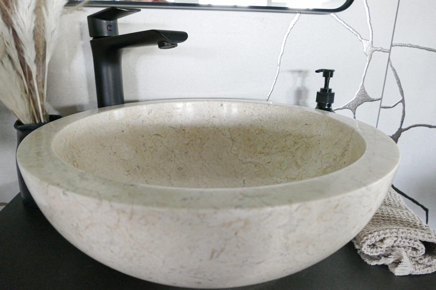 Beiges rundes Marmorbecken mit schwarzer Armatur