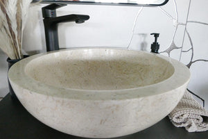 Beiges rundes Marmorbecken mit schwarzer Armatur